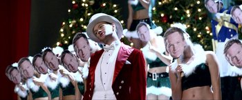 Movie still from “A Very Harold & Kumar Christmas” (2011), directed by Todd Strauss-Schulson – A man in a white hat and a red jacket is standing in front of a christmas tree; Medium shot, Over the shoulder angle