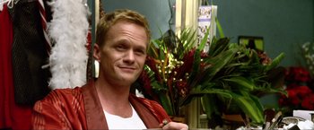 Movie still from “A Very Harold & Kumar Christmas” (2011), directed by Todd Strauss-Schulson – Neil patrick harris is smiling for the camera in front of some flowers; Close Up shot, Low angle