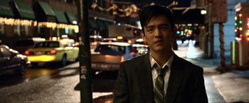 Movie still from “A Very Harold & Kumar Christmas” (2011), directed by Todd Strauss-Schulson – A man in a suit and tie standing in front of a busy street at night; Close Up shot, Over the shoulder angle