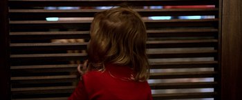 A little girl in a red jacket looking out a window