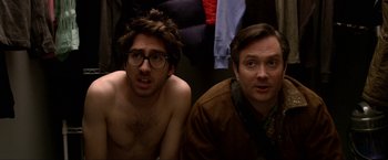 Movie still from “A Very Harold & Kumar Christmas” (2011), directed by Todd Strauss-Schulson – Two men sitting next to each other in front of a wall; Medium shot, Over the shoulder angle