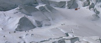 Movie still from “A View to a Kill” (1985), directed by John Glen – A group of people walking across a snow covered slope; Extreme Wide shot, High angle