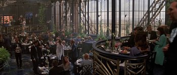 Movie still from “A View to a Kill” (1985), directed by John Glen – A group of people sitting at tables in a restaurant; Wide shot, Over the shoulder angle