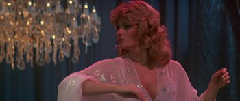 Movie still from “A View to a Kill” (1985), directed by John Glen – A woman in a white dress and a necklace in front of a chandelier; Medium shot, Low angle
