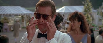 Movie still from “A View to a Kill” (1985), directed by John Glen – A person wearing a suit and sunglasses; Close Up shot, Over the shoulder angle