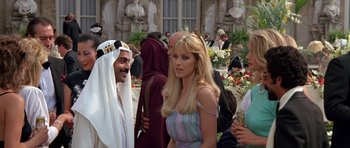 Movie still from “A View to a Kill” (1985), directed by John Glen – A woman standing next to a crowd of people in front of a building; Medium shot, Over the shoulder angle