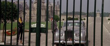 Movie still from “A View to a Kill” (1985), directed by John Glen – A man in a suit and a hat standing in front of an old car; Wide shot, Over the shoulder angle