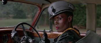 Movie still from “A View to a Kill” (1985), directed by John Glen – A woman in a uniform sitting in a car holding a gun; Close Up shot, Low angle