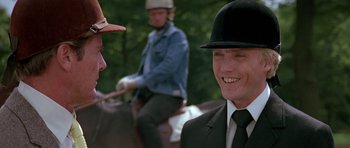 Movie still from “A View to a Kill” (1985), directed by John Glen – A man wearing a hat and a suit and tie; Close Up shot, Over the shoulder angle