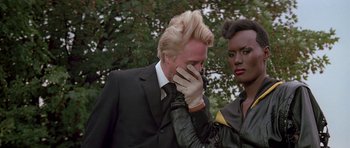 Movie still from “A View to a Kill” (1985), directed by John Glen – A man in a black suit and a woman in a black leather jacket; Close Up shot, Over the shoulder angle