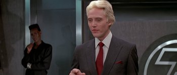 Movie still from “A View to a Kill” (1985), directed by John Glen – A man in a suit and tie standing in front of an elevator; Close Up shot, Low angle