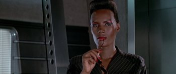 Movie still from “A View to a Kill” (1985), directed by John Glen – A man with red lipstick is holding a pair of glasses; Close Up shot, Low angle