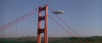 Movie still from “A View to a Kill” (1985), directed by John Glen – An airliner is flying over a bridge in a city; Extreme Wide shot, Low angle