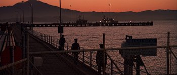 Movie still from “A View to a Kill” (1985), directed by John Glen – A group of people standing on a pier at sunset; Extreme Wide shot, High angle