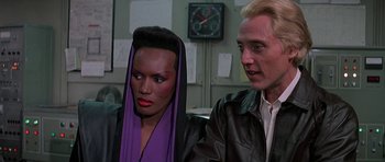 Movie still from “A View to a Kill” (1985), directed by John Glen – A man and a woman are sitting next to each other; Close Up shot, Over the shoulder angle