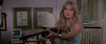 Movie still from “A View to a Kill” (1985), directed by John Glen – A woman holding a gun in a room with a lamp on the wall; Close Up shot, Over the shoulder angle