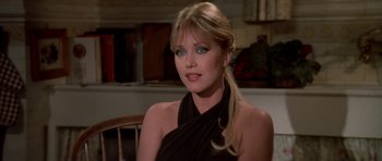 Movie still from “A View to a Kill” (1985), directed by John Glen – A woman in a black dress sitting in front of a wooden chair; Close Up shot, Over the shoulder angle