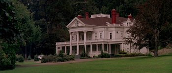 Movie still from “A View to a Kill” (1985), directed by John Glen – A large white house sitting on top of a green field; Extreme Wide shot, Low angle
