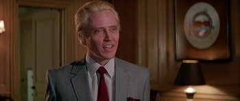Movie still from “A View to a Kill” (1985), directed by John Glen – A man in a suit and red tie smiling; Close Up shot, Over the shoulder angle