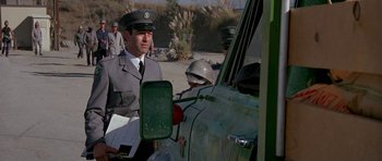 Movie still from “A View to a Kill” (1985), directed by John Glen – A man in a military uniform standing next to a car; Medium shot, Low angle