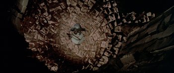 Movie still from “A View to a Kill” (1985), directed by John Glen – A man is sitting in a pile of money; Extreme Wide shot, Overhead angle
