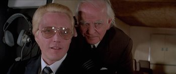 Movie still from “A View to a Kill” (1985), directed by John Glen – A man and a man in a suit posing for a picture; Close Up shot, Low angle