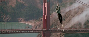 Movie still from “A View to a Kill” (1985), directed by John Glen – A man hanging from a rope over a bridge; Extreme Wide shot, Low angle