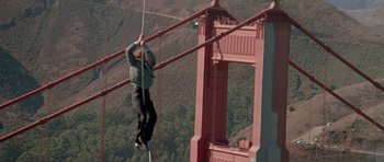 Movie still from “A View to a Kill” (1985), directed by John Glen – A man hanging from the side of a tall bridge; Wide shot, Low angle