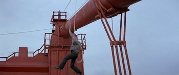 Movie still from “A View to a Kill” (1985), directed by John Glen – A man hanging from a rope attached to a metal structure; Extreme Wide shot, High angle