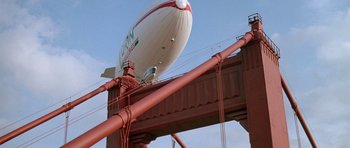 Movie still from “A View to a Kill” (1985), directed by John Glen – A large white and red balloon sitting on top of a bridge; Extreme Wide shot, Low angle