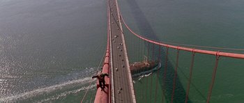 Movie still from “A View to a Kill” (1985), directed by John Glen – A man on the side of a bridge with a boat in the background; Extreme Wide shot, High angle