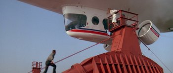 Movie still from “A View to a Kill” (1985), directed by John Glen – Two people are climbing down the stairs of an airplane; Extreme Wide shot, Low angle