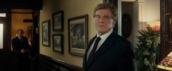 Movie still from “A Walk in the Woods” (2015), directed by Ken Kwapis – A man wearing a suit and tie standing in front of a painting; Medium shot, Low angle