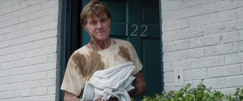 Movie still from “A Walk in the Woods” (2015), directed by Ken Kwapis – An older man holding a bunch of folded towels outside of a house; Medium shot, Low angle