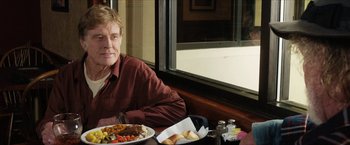 Movie still from “A Walk in the Woods” (2015), directed by Ken Kwapis – A man sitting in front of a plate of food; Medium shot, Over the shoulder angle