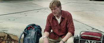 Movie still from “A Walk in the Woods” (2015), directed by Ken Kwapis – A man sitting on the ground with a bag of luggage next to him; Medium shot, Low angle