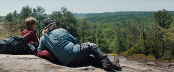 Movie still from “A Walk in the Woods” (2015), directed by Ken Kwapis – A man sitting on top of a rock on top of a mountain; Wide shot, Over the shoulder angle