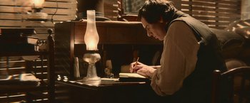 Movie still from “Abraham Lincoln: Vampire Hunter” (2012), directed by Timur Bekmambetov – A person writing in a notebook near a lamp; Medium shot, High angle