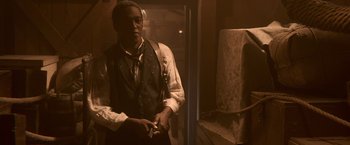 Movie still from “Abraham Lincoln: Vampire Hunter” (2012), directed by Timur Bekmambetov – A man standing in a dimly - lit room holding a cigarette; Medium shot, Low angle