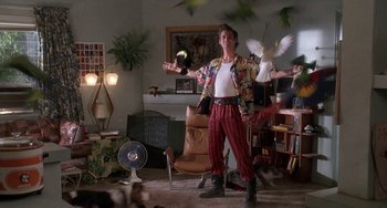 Movie still from “Ace Ventura: Pet Detective” (1994), directed by Tom Shadyac – A man standing in a living room holding a white bird; Wide shot, Low angle