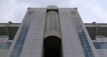 Movie still from “Ace Ventura: Pet Detective” (1994), directed by Tom Shadyac – A tall white building with a large window; Extreme Wide shot, Low angle