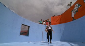 Movie still from “Ace Ventura: Pet Detective” (1994), directed by Tom Shadyac – A group of people standing on top of a blue building; Extreme Wide shot, Low angle