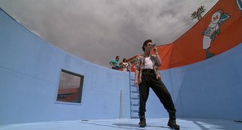 Movie still from “Ace Ventura: Pet Detective” (1994), directed by Tom Shadyac – A man singing into a microphone on a stage; Wide shot, Low angle