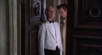 Movie still from “Ace Ventura: Pet Detective” (1994), directed by Tom Shadyac – A man standing next to another man in front of an open door; Medium shot, Over the shoulder angle