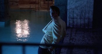 Movie still from “Ace Ventura: Pet Detective” (1994), directed by Tom Shadyac – A man in a white jacket standing next to a body of water at night; Medium shot, Over the shoulder angle