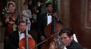 Movie still from “Ace Ventura: Pet Detective” (1994), directed by Tom Shadyac – A group of men in tuxedos playing musical instruments; Medium shot, Over the shoulder angle