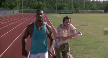 Movie still from “Ace Ventura: Pet Detective” (1994), directed by Tom Shadyac – A man and a woman are running on a track; Medium shot, Over the shoulder angle