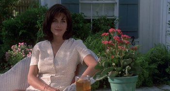 Movie still from “Ace Ventura: Pet Detective” (1994), directed by Tom Shadyac – A woman sitting in front of a flower pot with a drink; Medium shot, Low angle