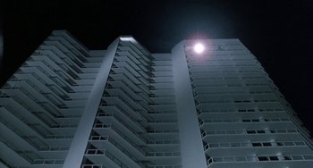 Movie still from “Ace Ventura: Pet Detective” (1994), directed by Tom Shadyac – The sun is shining in the dark sky above a tall building; Extreme Wide shot, Low angle