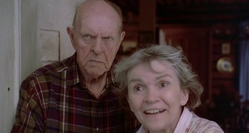 Movie still from “Ace Ventura: Pet Detective” (1994), directed by Tom Shadyac – An older man and a younger woman posing for a picture; Close Up shot, Low angle